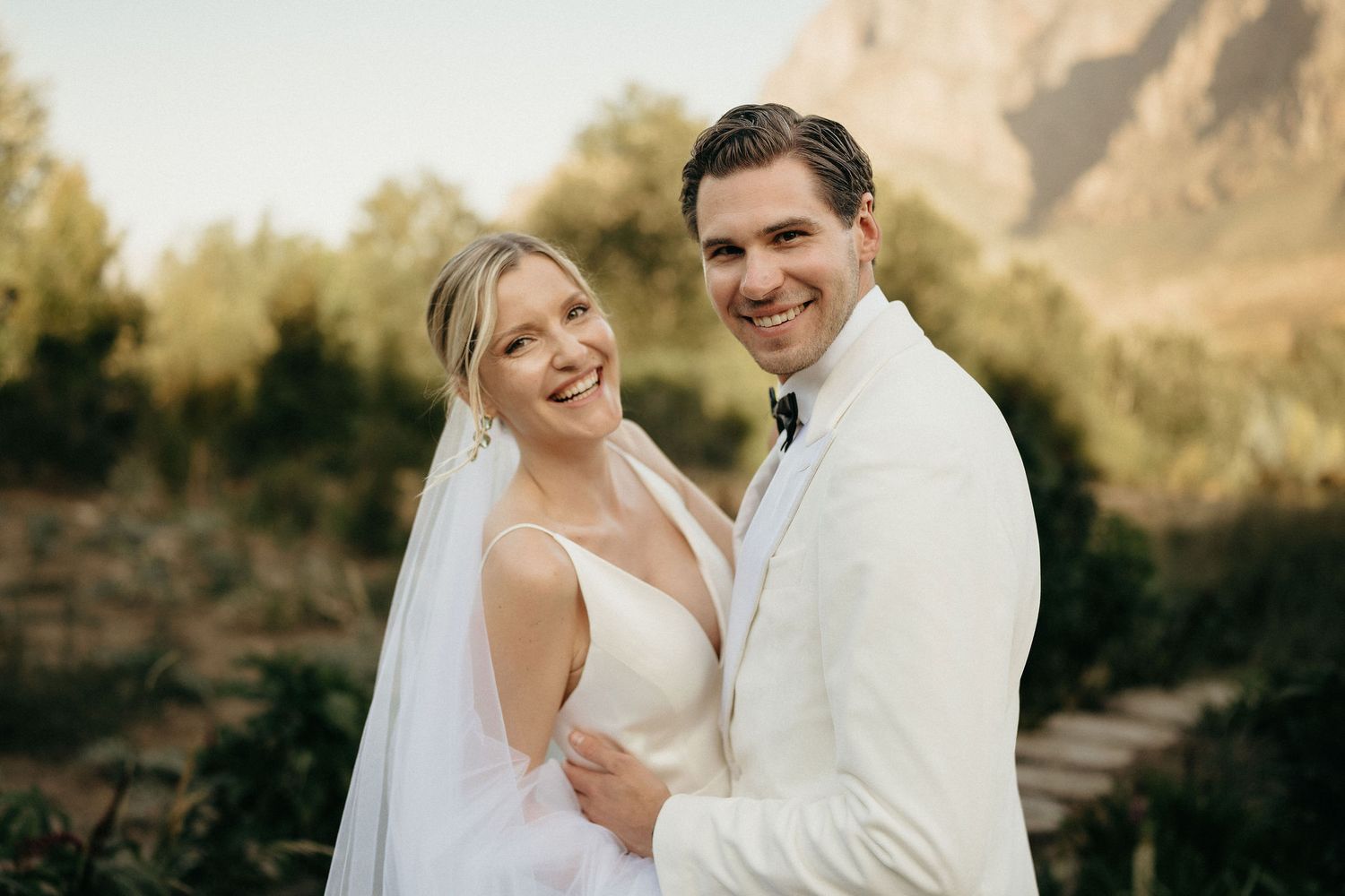 A joyful wedding couple embraces outdoors in a desert landscape during golden hour.