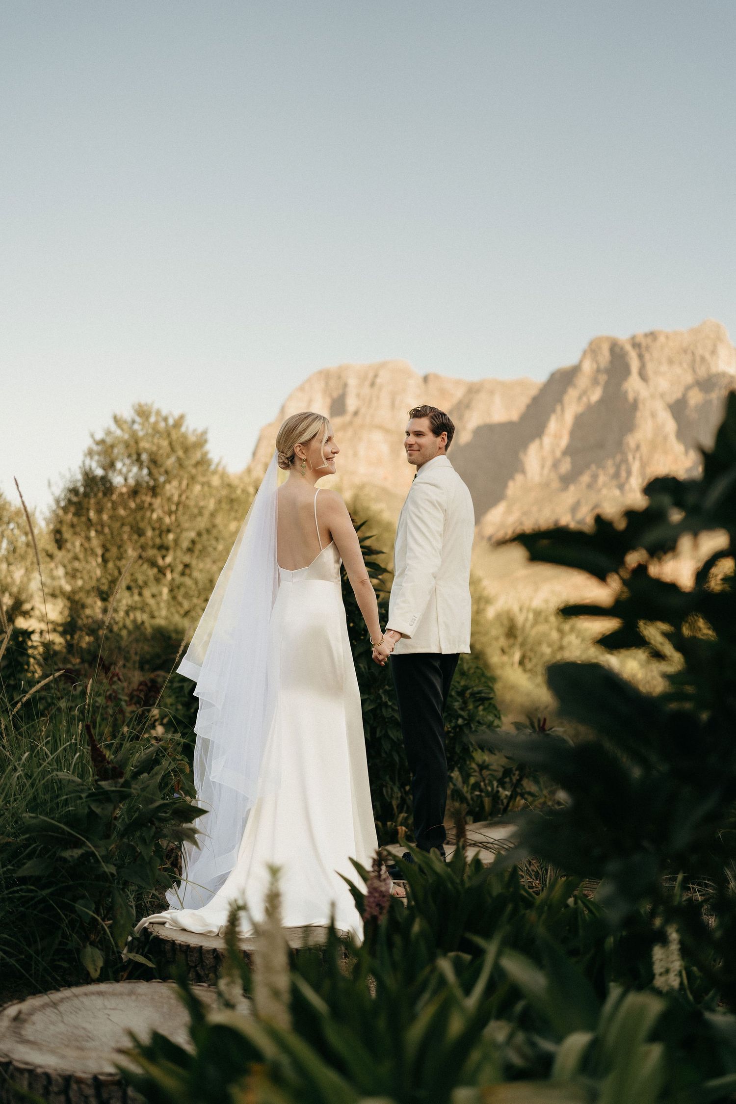 A couple shares an intimate moment against a backdrop of majestic mountain cliffs during their outdoor desert wedding.