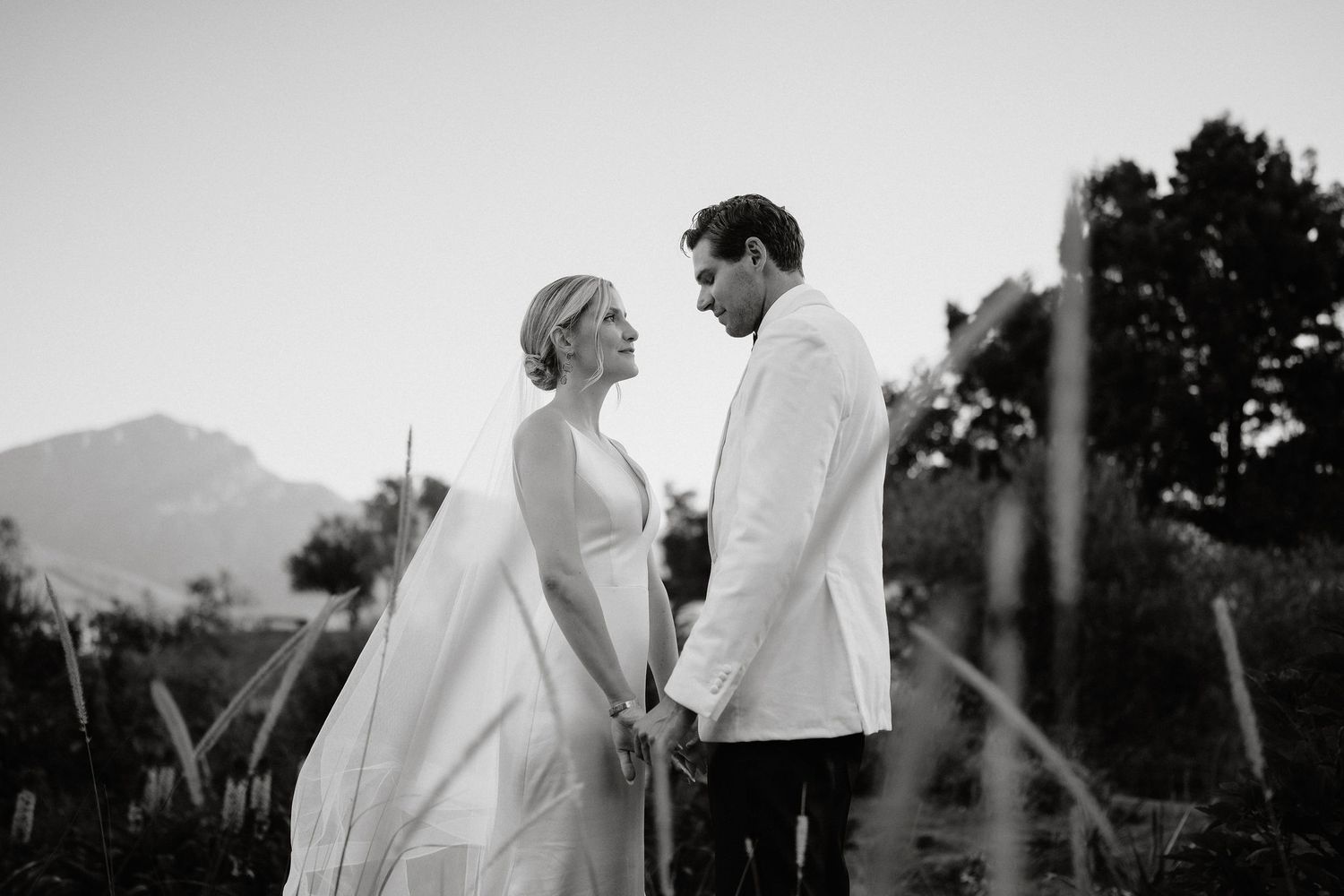 A romantic couple in wedding attire shares tender moments at sunset in a scenic outdoor setting.