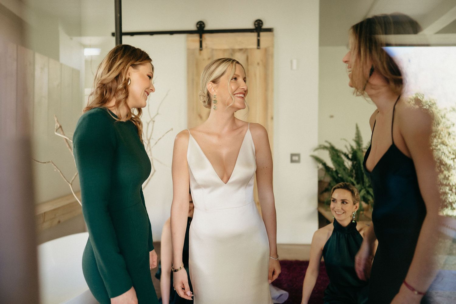Three women in elegant dresses, one in emerald green, one in white, and one in black, share a joyful moment together.