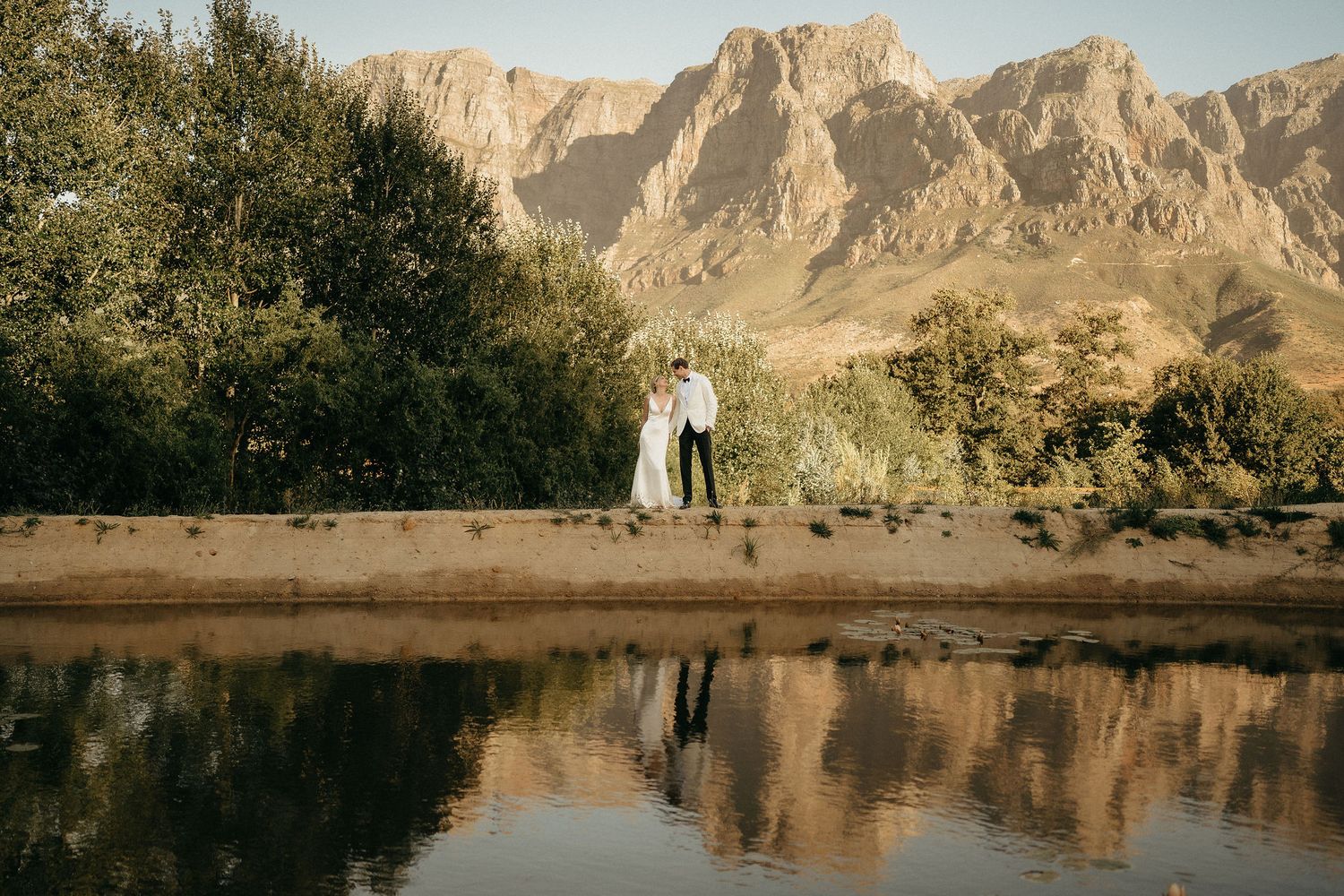 Desert landscape with dramatic mountain cliffs reflected in still water during sunset.