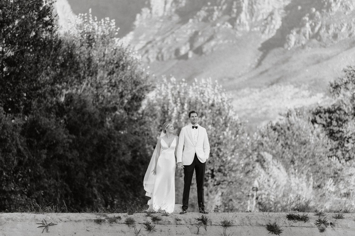 A black and white wedding photo series shows couples posing in an outdoor garden setting with mountain landscapes.