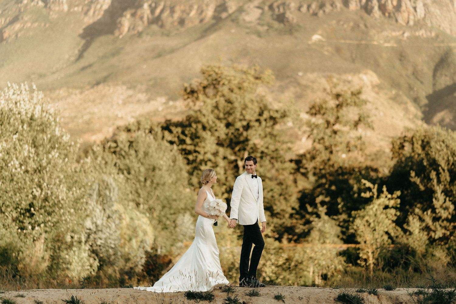 A scenic desert mountain wedding ceremony with a white-gowned bride and suited groom surrounded by rugged terrain.
