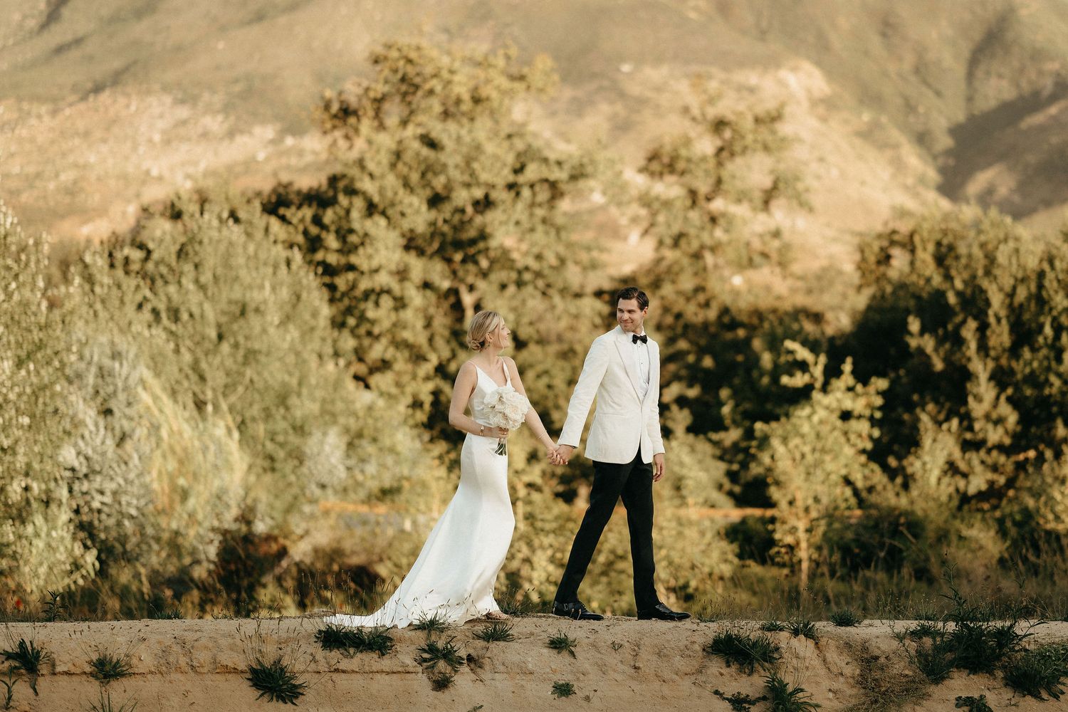 A couple poses together in front of scenic desert mountains during golden hour sunset for wedding photos.