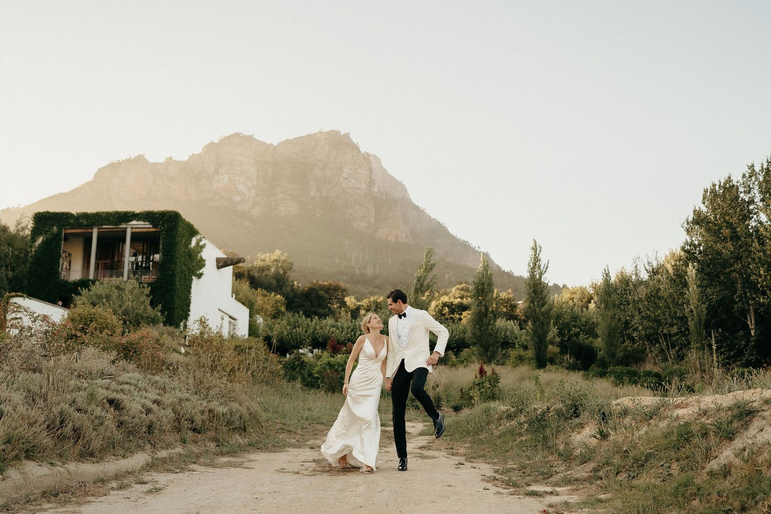 A couple walks along a scenic mountain path during a wedding photoshoot with dramatic landscape views.