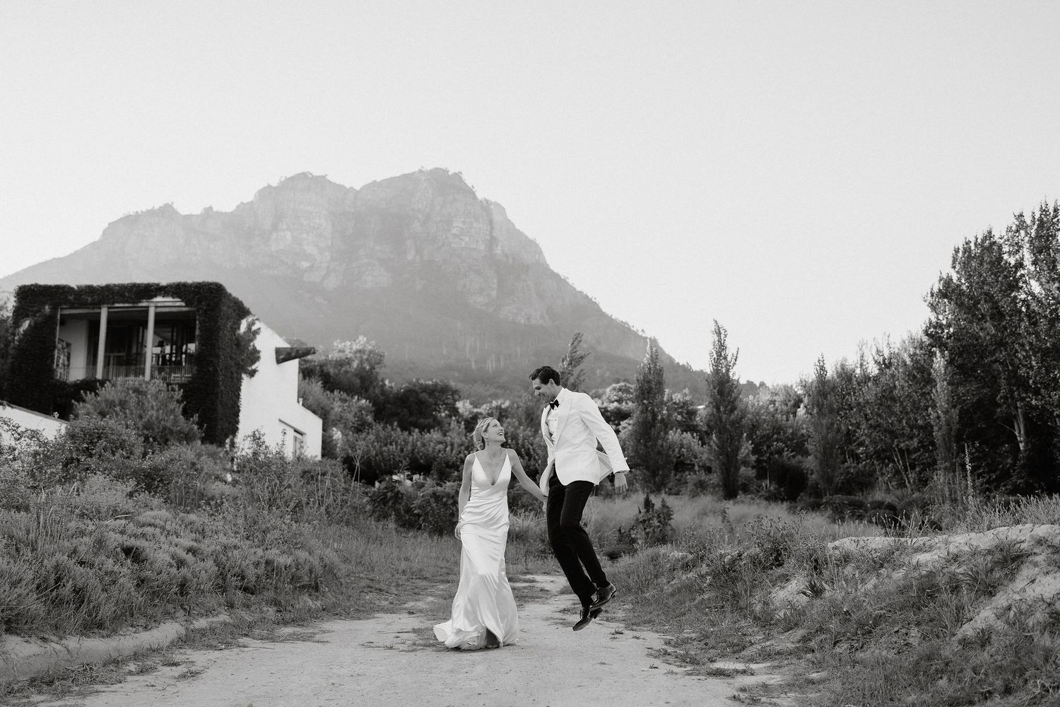 A black and white panoramic landscape photograph showing a mountain range and rural buildings in the distance.