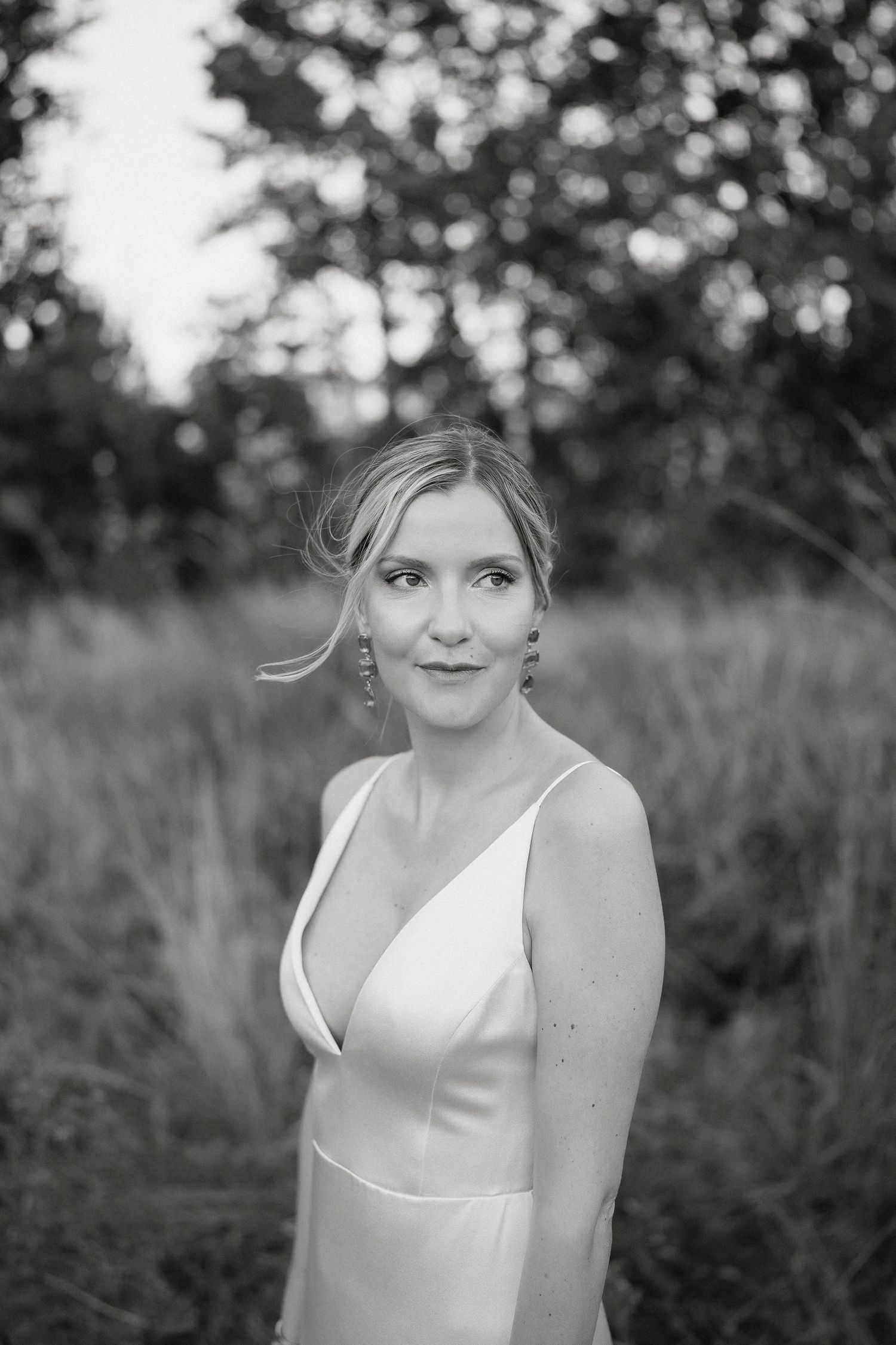Black and white portrait of someone wearing a white sleeveless top in an outdoor setting with bokeh background.