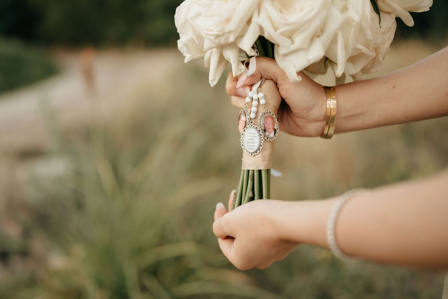 Hands holding white wedding bouquet wrapped with pearl and crystal embellished ribbon detail.