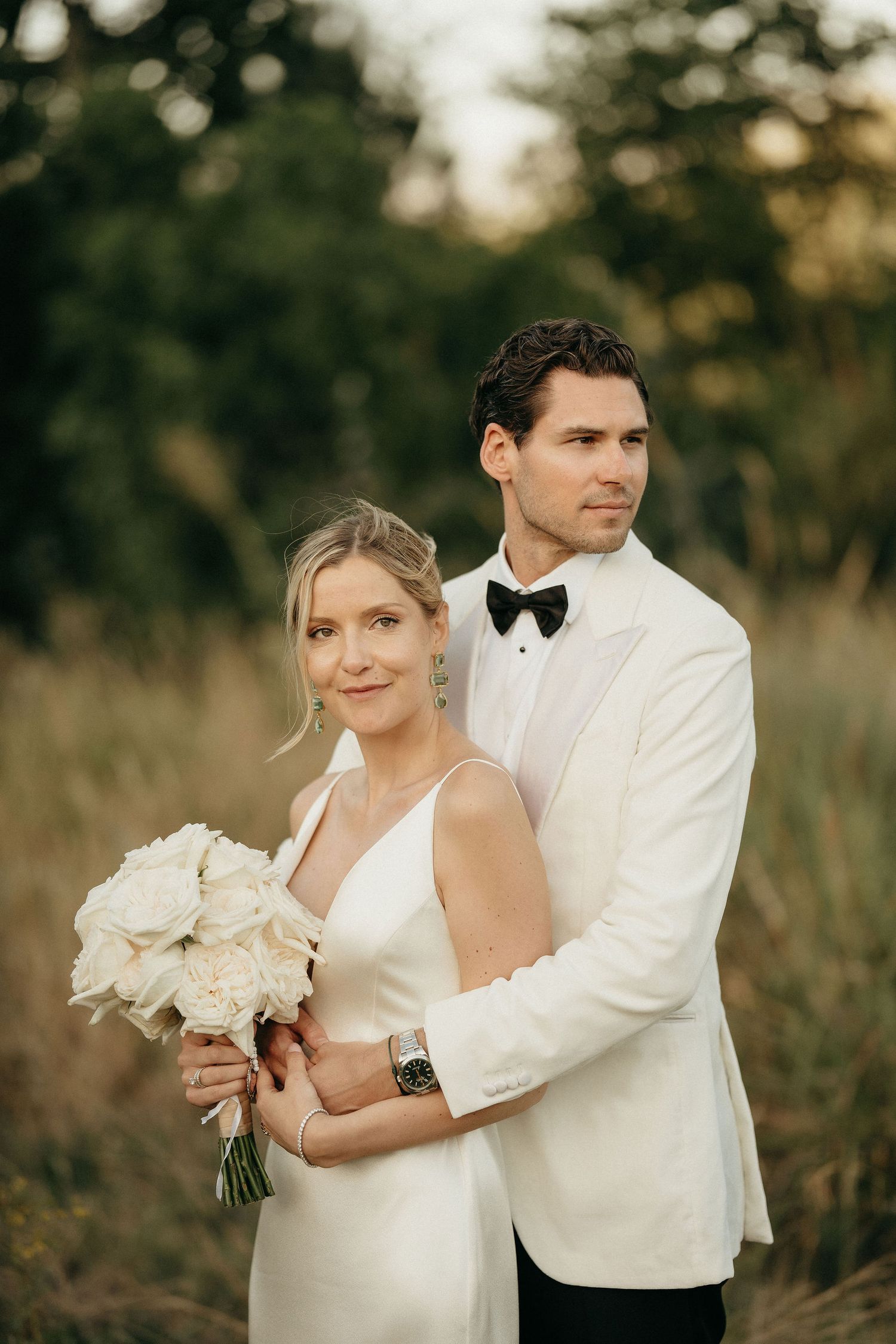 A romantic wedding portrait series shows a couple in white attire embracing in a sunlit outdoor field with a bouquet.