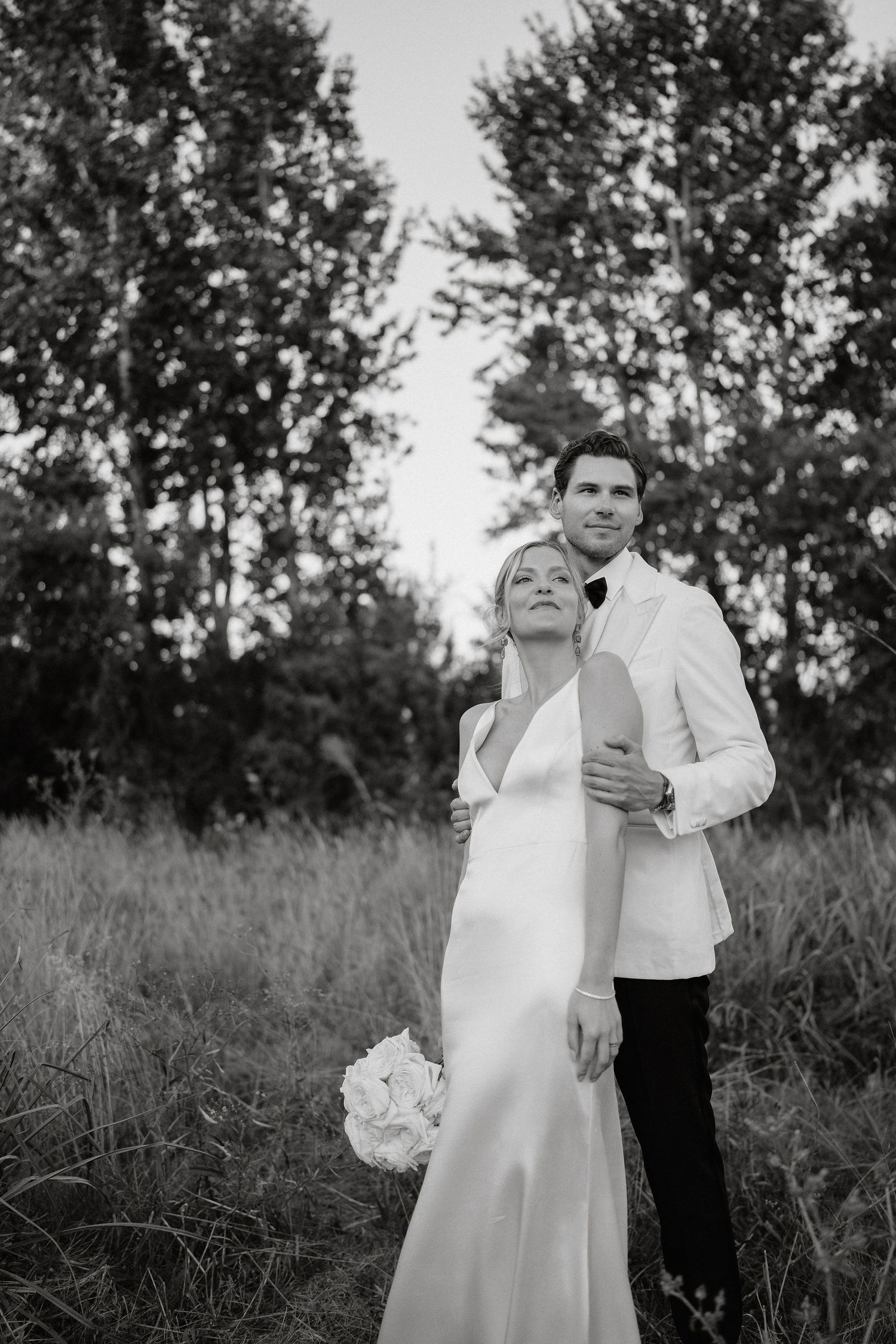 A romantic black and white photo sequence of a couple dancing in a field with trees in the background.