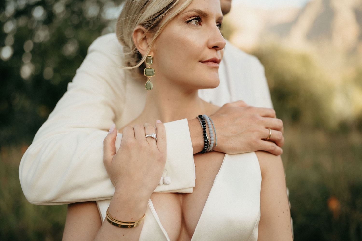 A bride in an elegant white sweater poses thoughtfully in a romantic outdoor setting during golden hour.