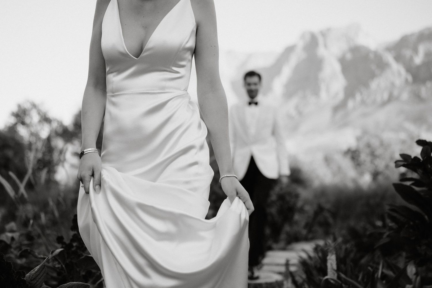 A bride in a white wedding dress poses outdoors with mountains and greenery in the background.