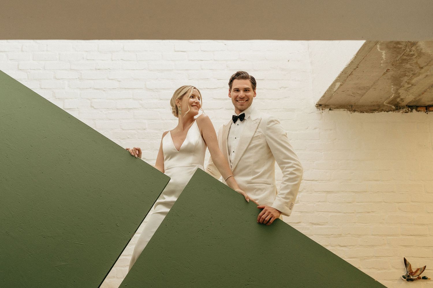 A couple in wedding attire embraces on a beach with cliffs and ocean waves in the background.