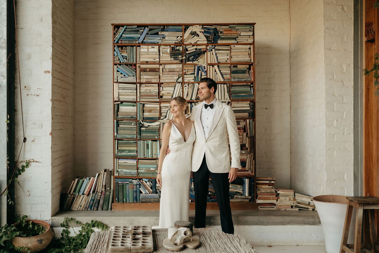 A person in white stands in a rustic room filled with vintage books and records on wooden shelves.