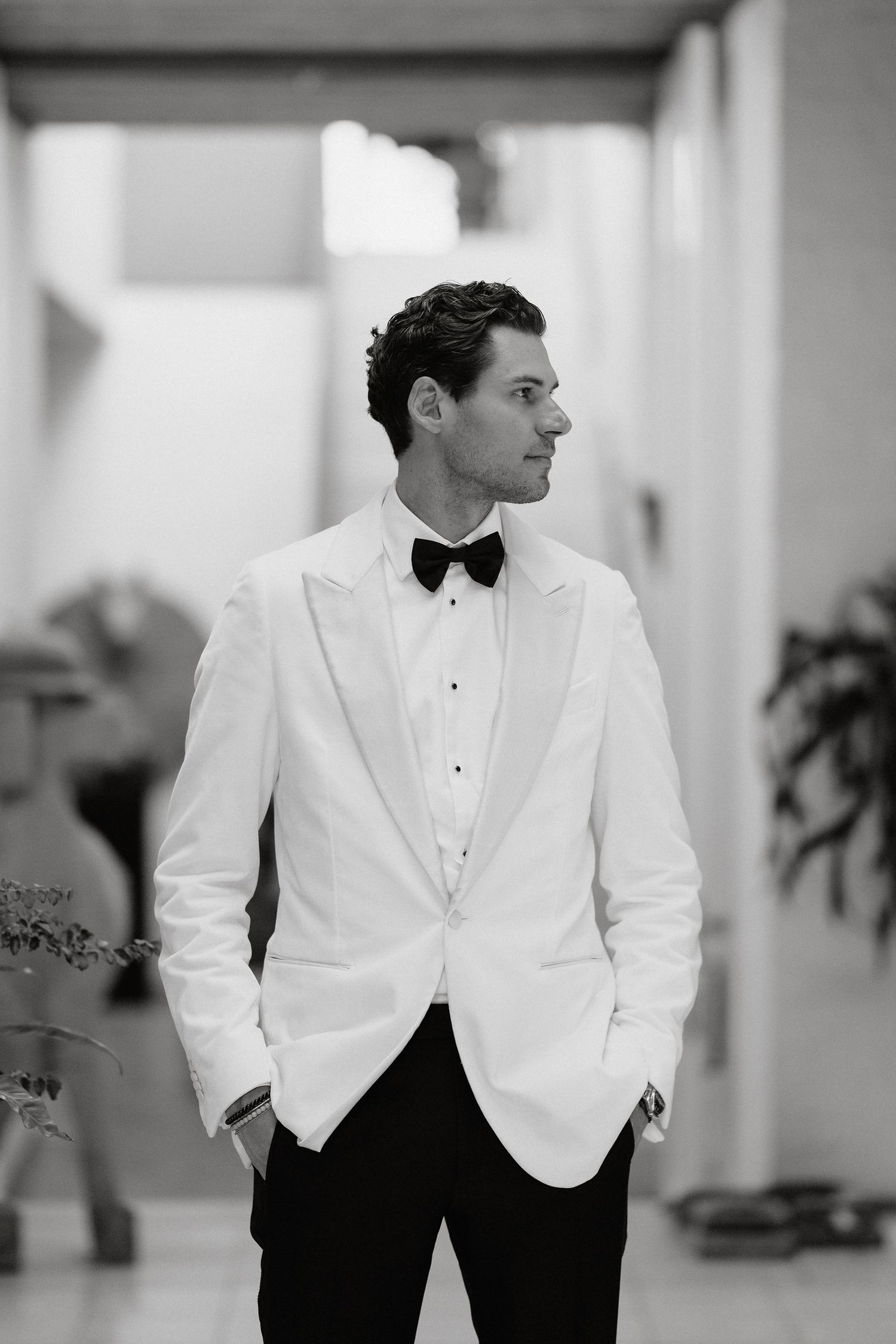 A black and white photo series showing someone in a white tuxedo jacket and black pants in various elegant poses.