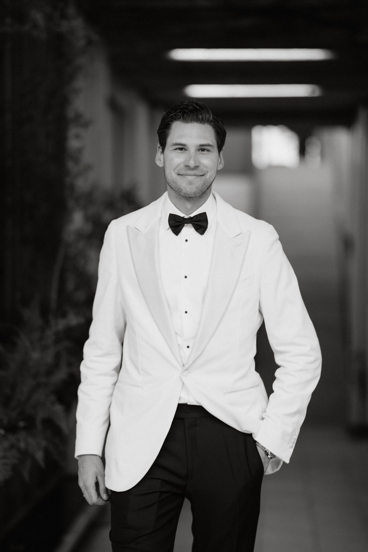 A man in a formal white dinner jacket and black bow tie poses for a series of elegant black and white photos.