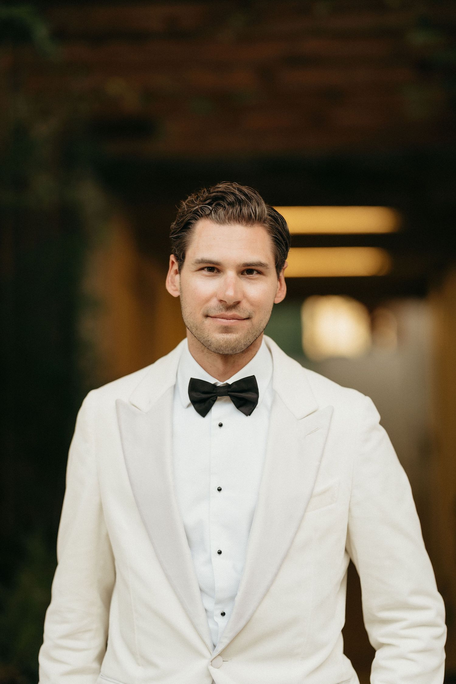 A person wearing a white tuxedo jacket and black bow tie in a formal portrait series.