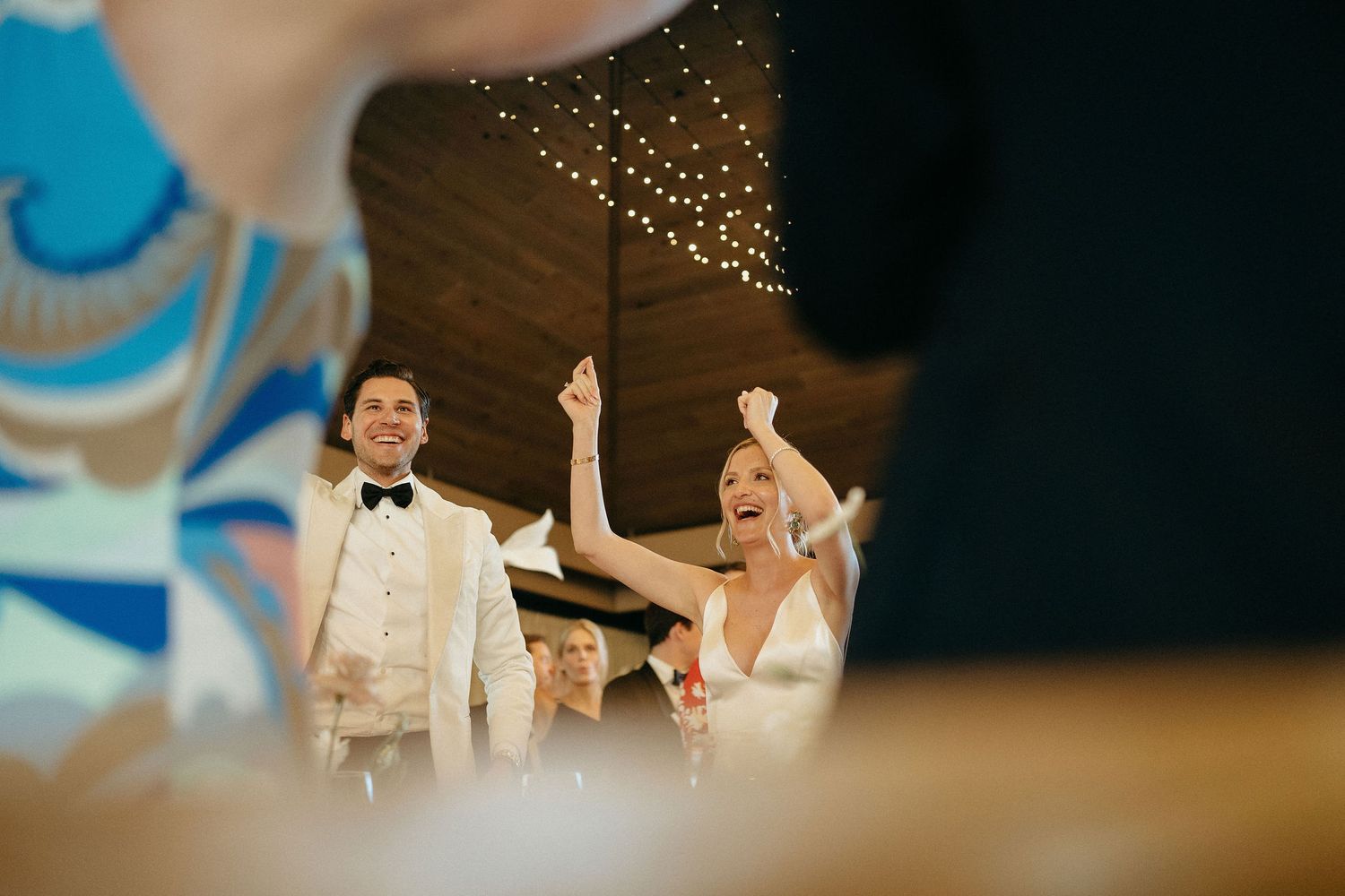 Wedding guests throw sparklers in celebration at an evening reception as the newlyweds dance under twinkling lights.
