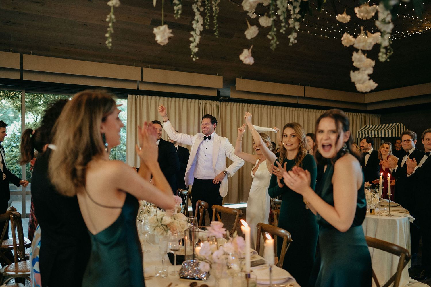 People dance and celebrate at an elegant wedding reception decorated with hanging white paper flowers.