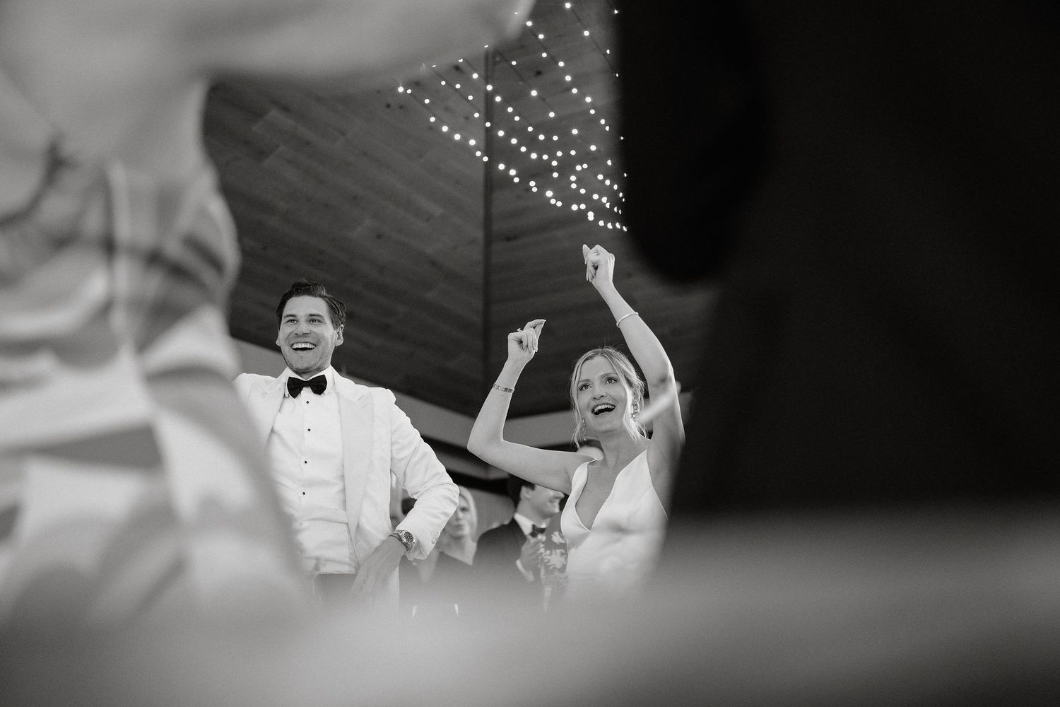 A black and white photo of a couple dancing and celebrating under sparkling lights at their wedding reception.