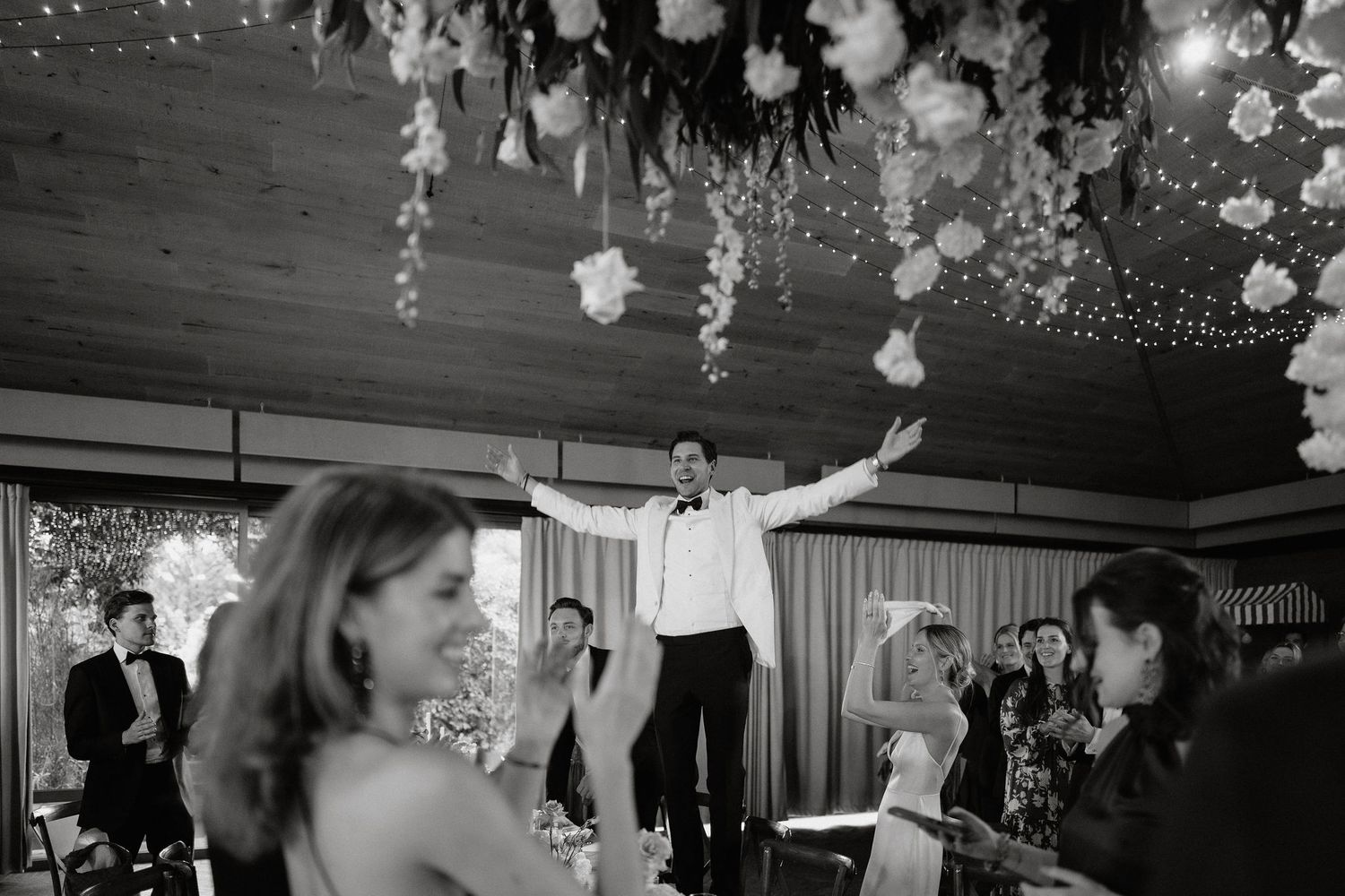 Black and white photos showing couples dancing at an elegant wedding reception with hanging floral decorations.