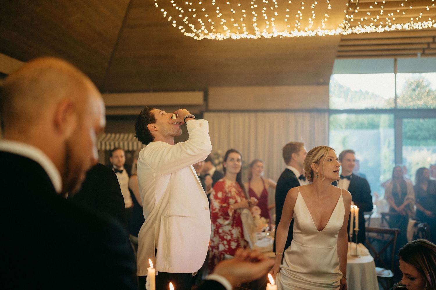 Wedding reception guests dance and celebrate under twinkling string lights in an elegant indoor venue.