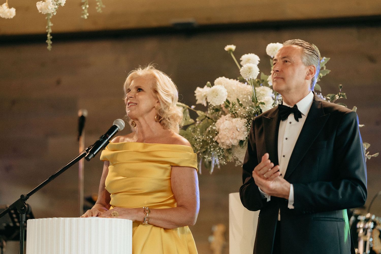 Wedding guests in formal attire enjoy a reception celebration with yellow dresses and black tuxedos.