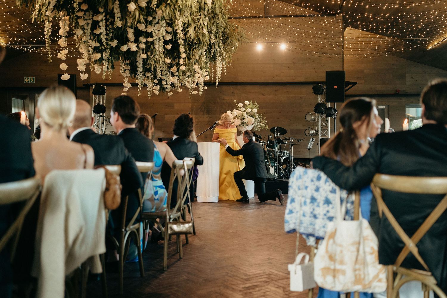 Wedding reception guests dancing and celebrating under crystal chandeliers in a rustic barn venue.