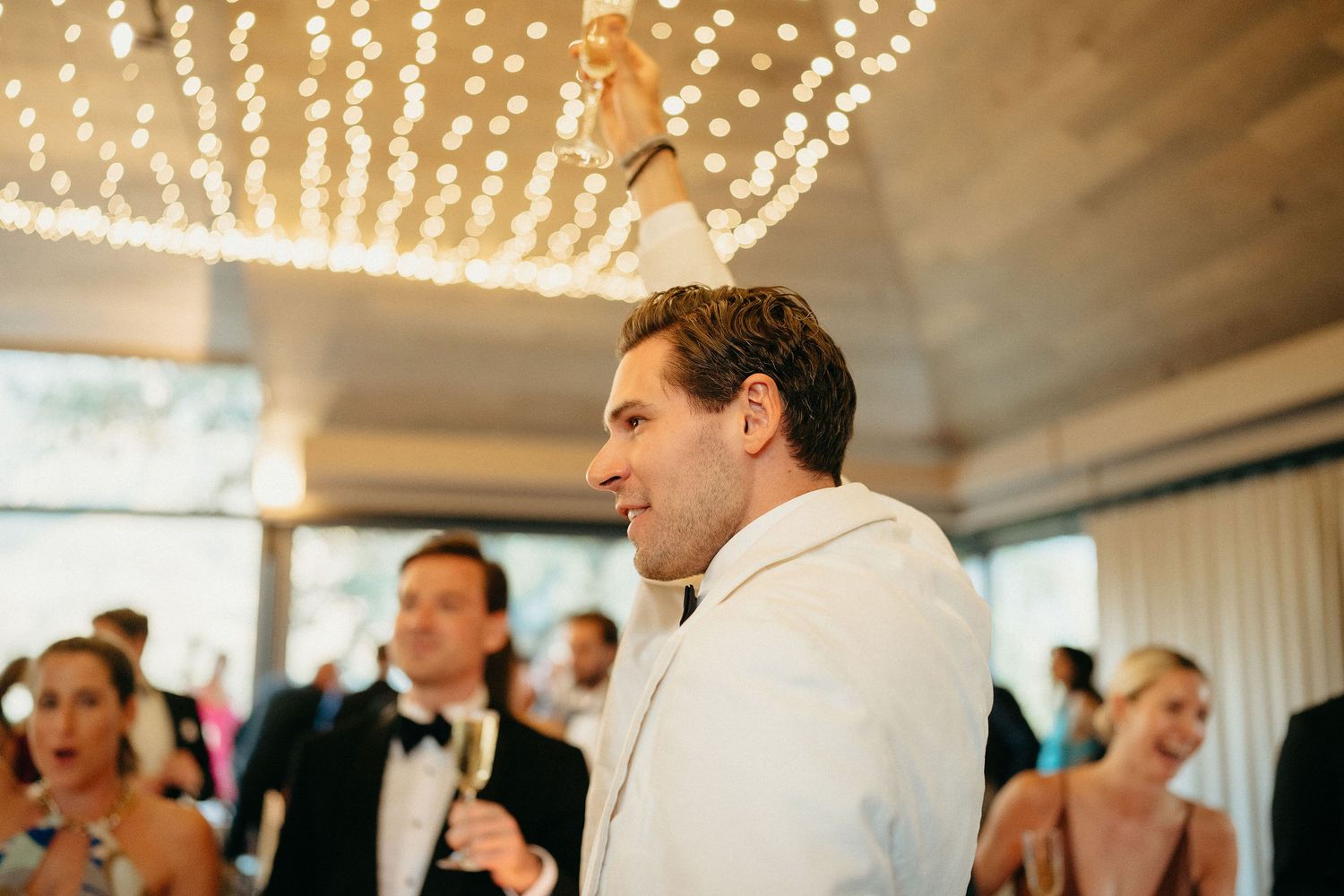 A wedding reception dance floor with string lights overhead as guests celebrate and dance together.