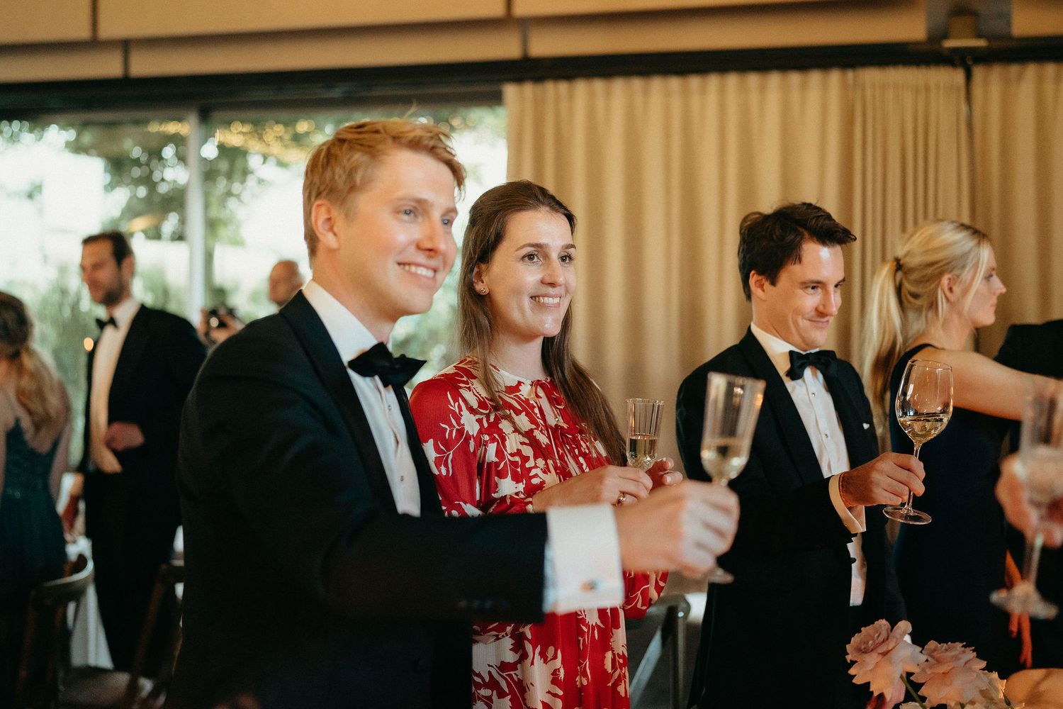 Wedding guests in formal attire raise champagne glasses during an elegant reception celebration.