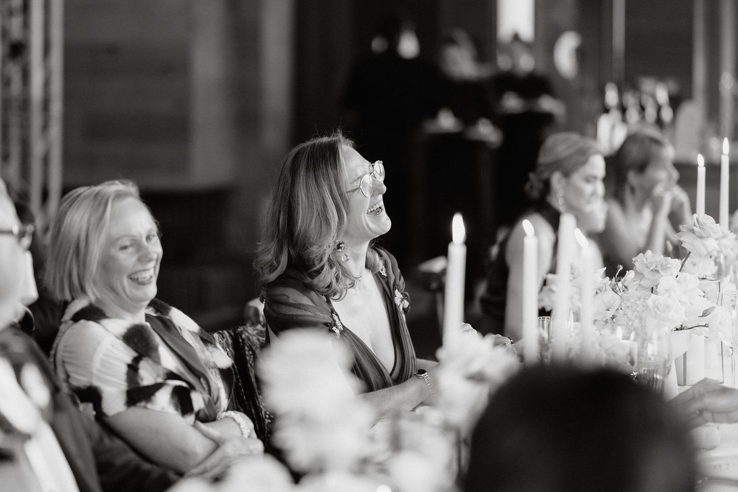 Black and white candid photo of guests laughing together at an elegant dinner party or reception.