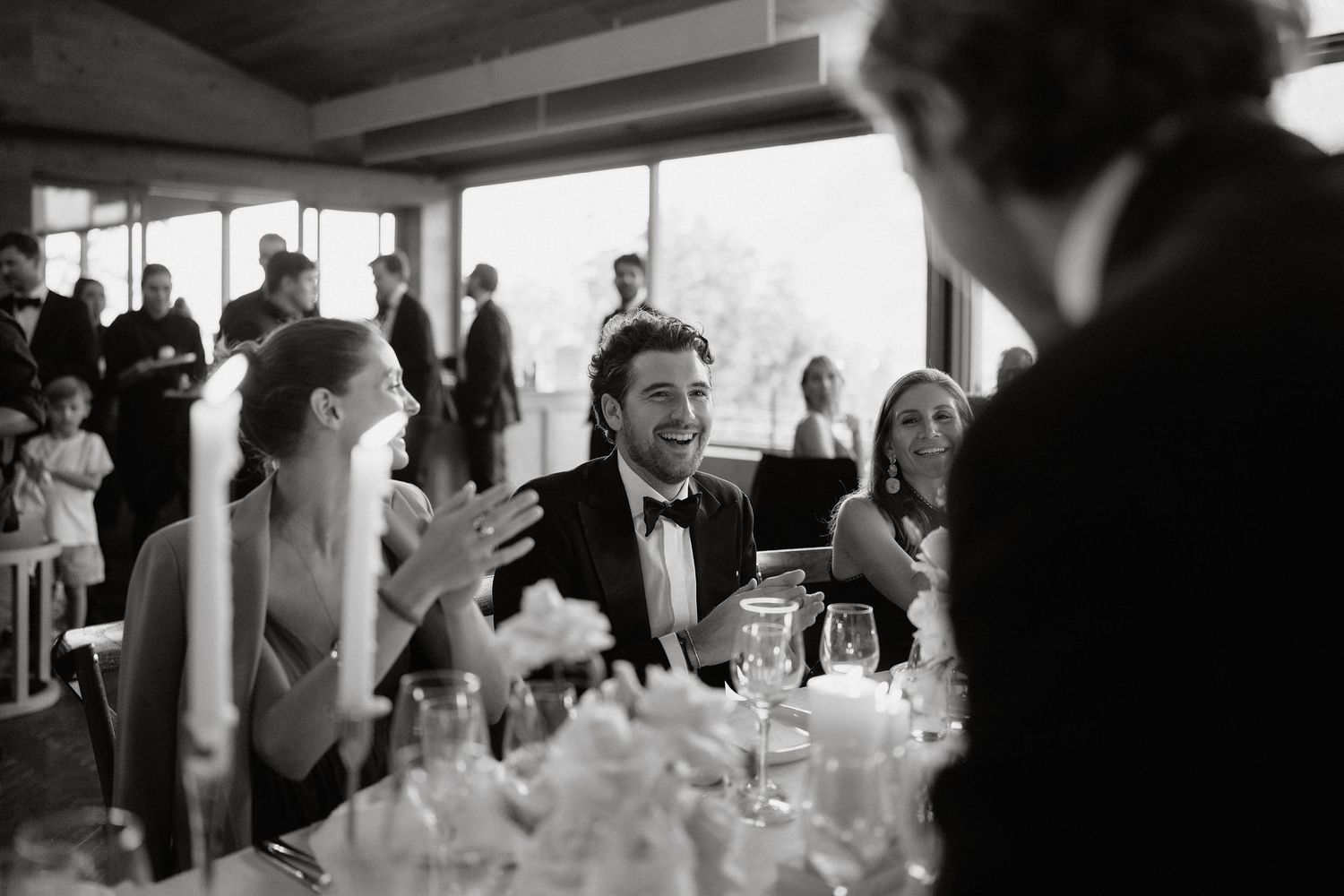 Wedding guests dance and celebrate together on a black and white tiled dance floor at an indoor reception.