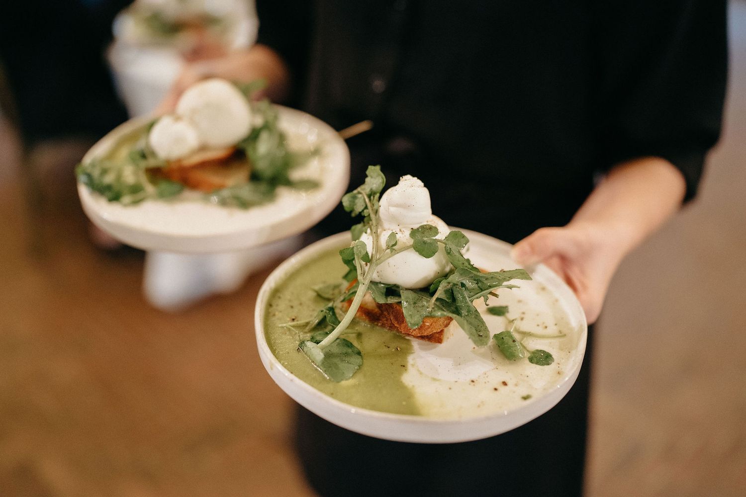 A close-up view of a creamy white sauce being drizzled over a plated dish with fresh herbs and garnishes.