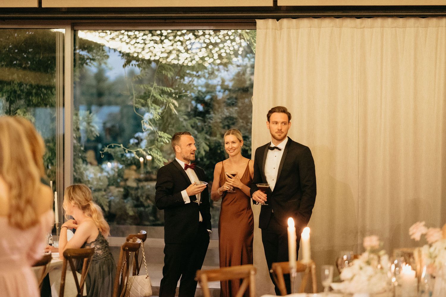 Wedding guests dance and celebrate under twinkling lights at an elegant indoor reception venue.