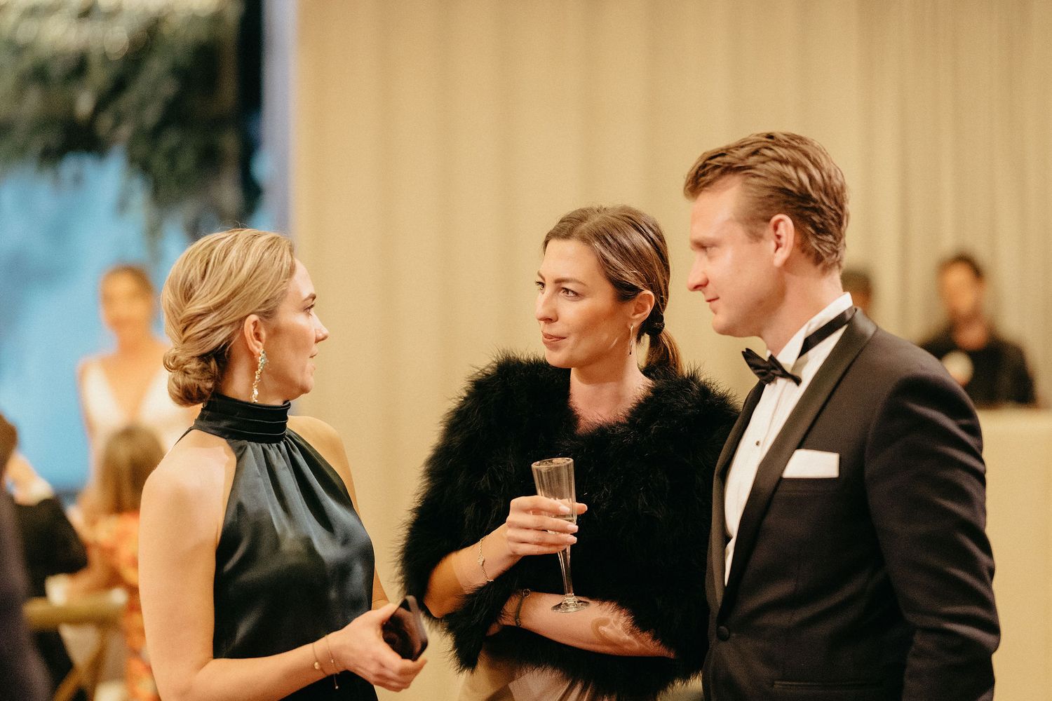 People in formal attire socialize at an elegant event with champagne glasses and evening wear.
