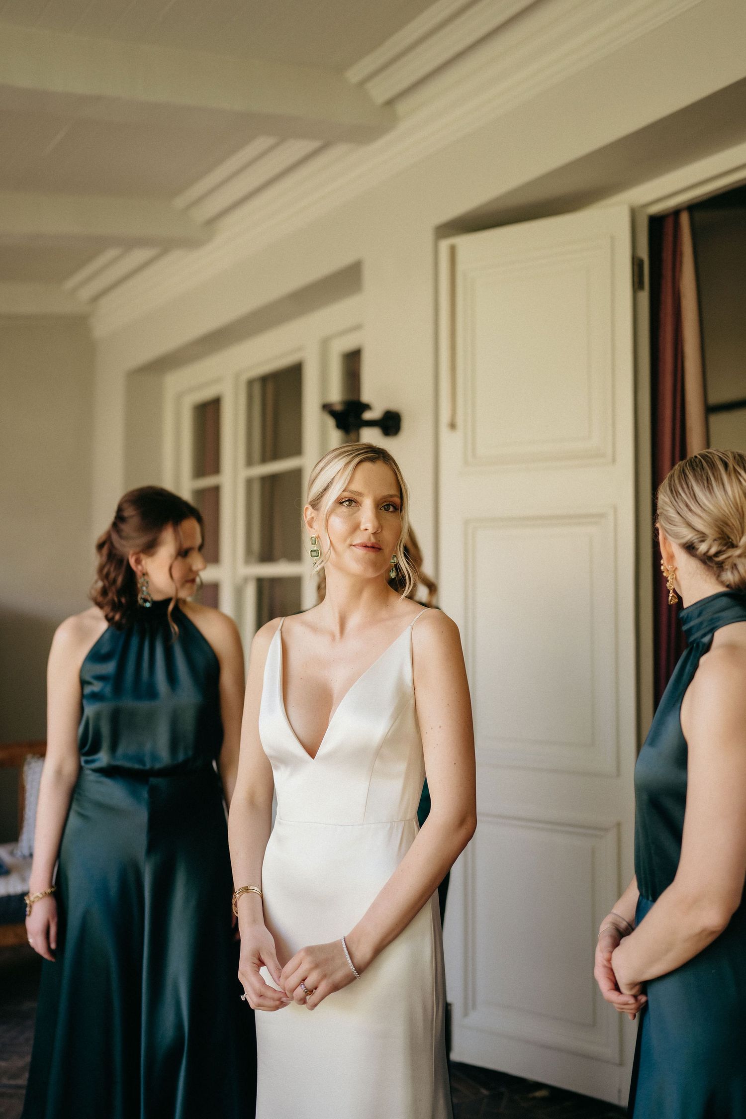 A group of women in formal attire stand together, with one wearing a white dress and others in dark green gowns.