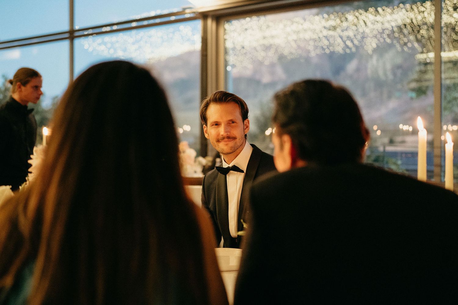 Wedding guests celebrate and dance during an elegant reception with scenic mountain views through large windows.