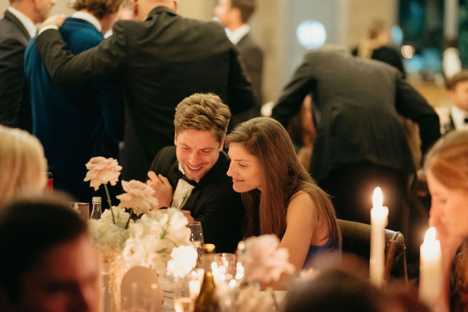 Elegant candlelit wedding reception tables decorated with white floral centerpieces and glowing taper candles.