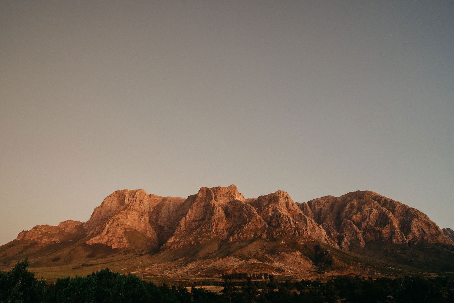 Rugged mountain peaks glow with warm orange light during sunset in a dramatic desert landscape.