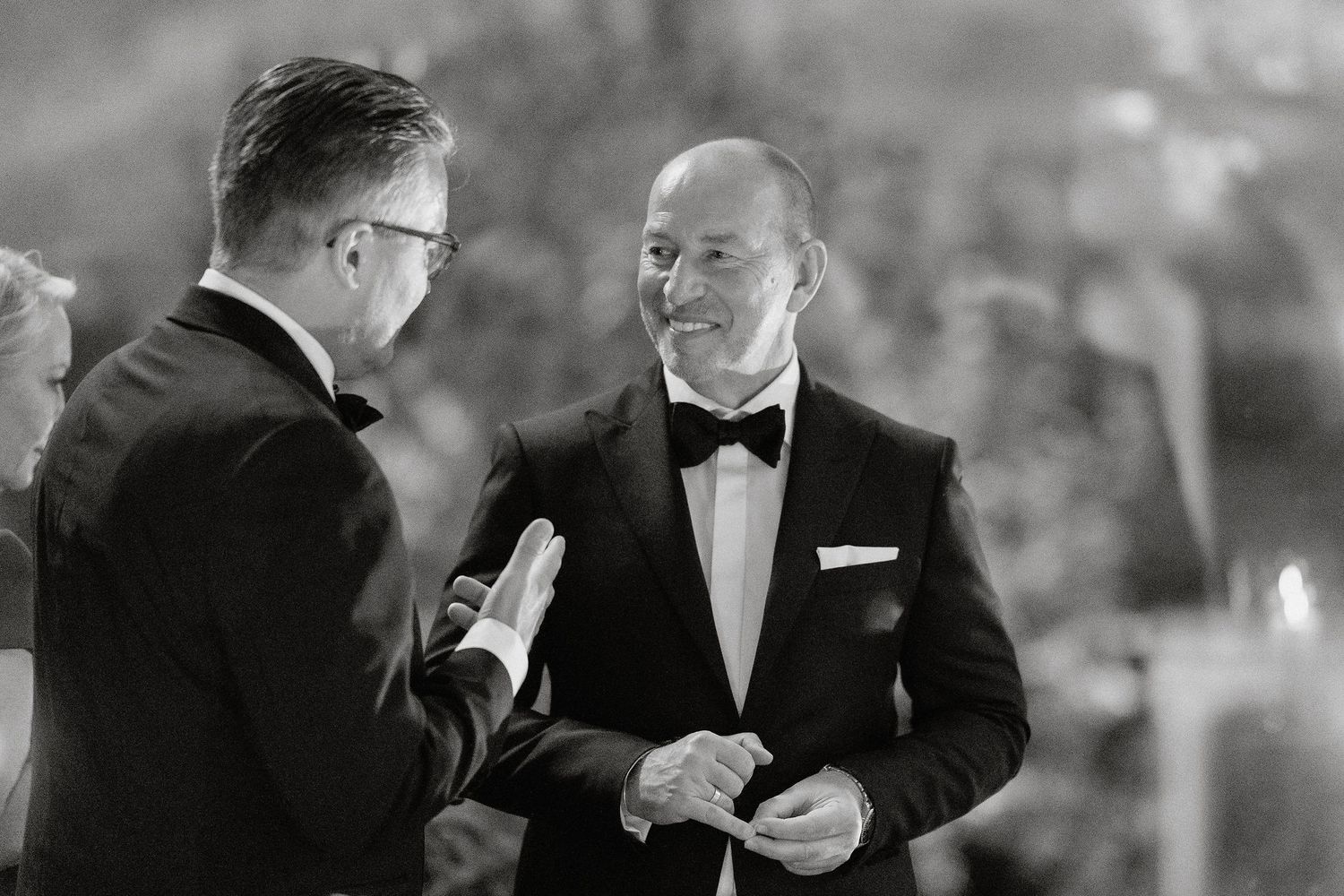 A group of people in formal black tie attire gather together for conversation at an elegant event.