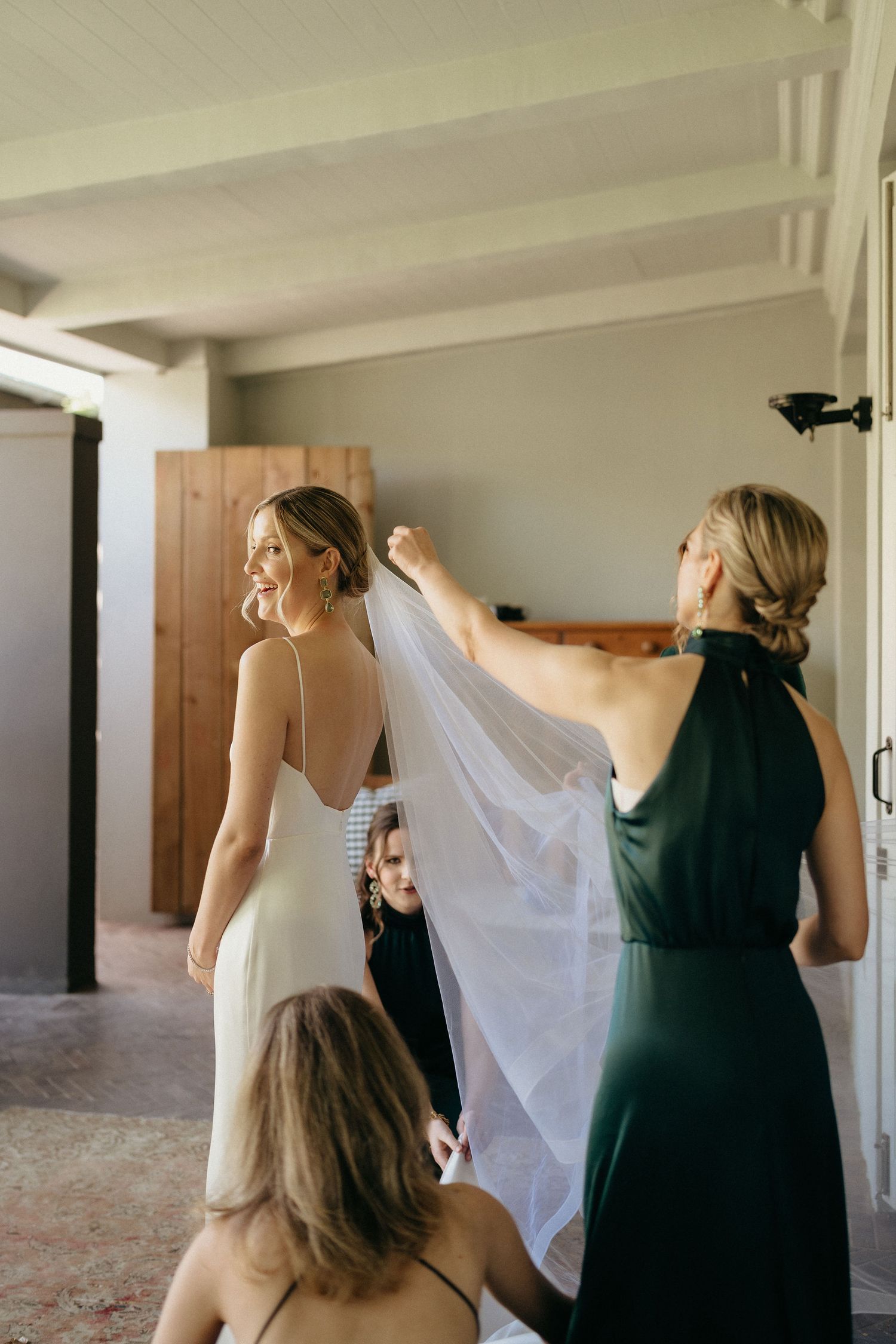 Three sequential photos show people helping adjust a flowing white veil in an indoor venue with pillars.