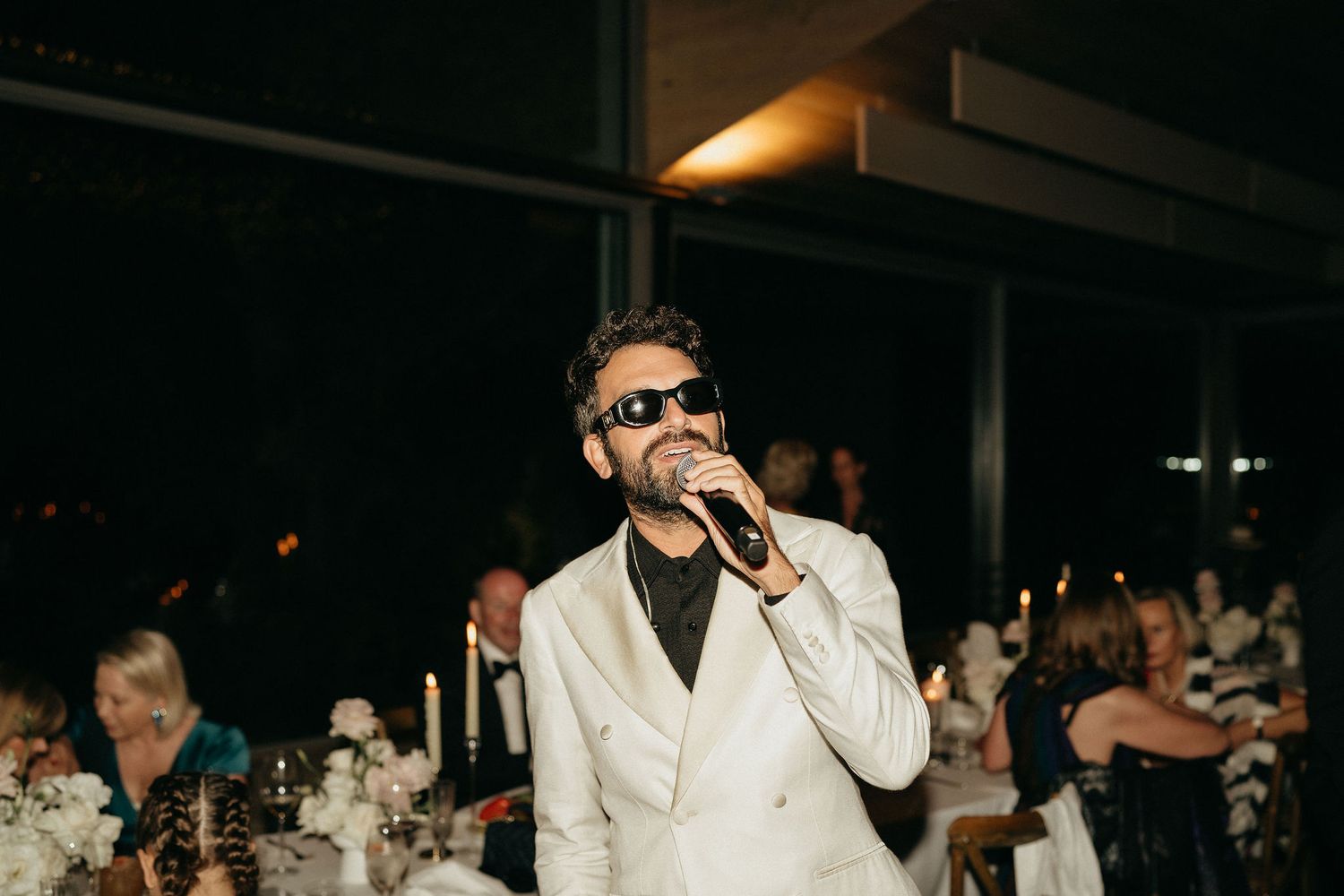 A performer in a white suit and sunglasses entertains a crowd at a nighttime event.