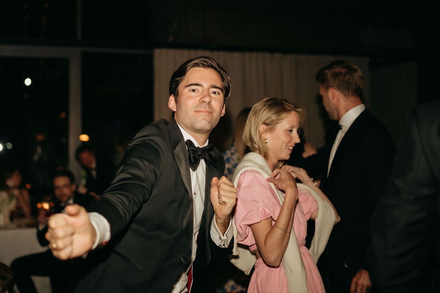 People dancing and mingling at a dimly lit formal event or wedding reception.