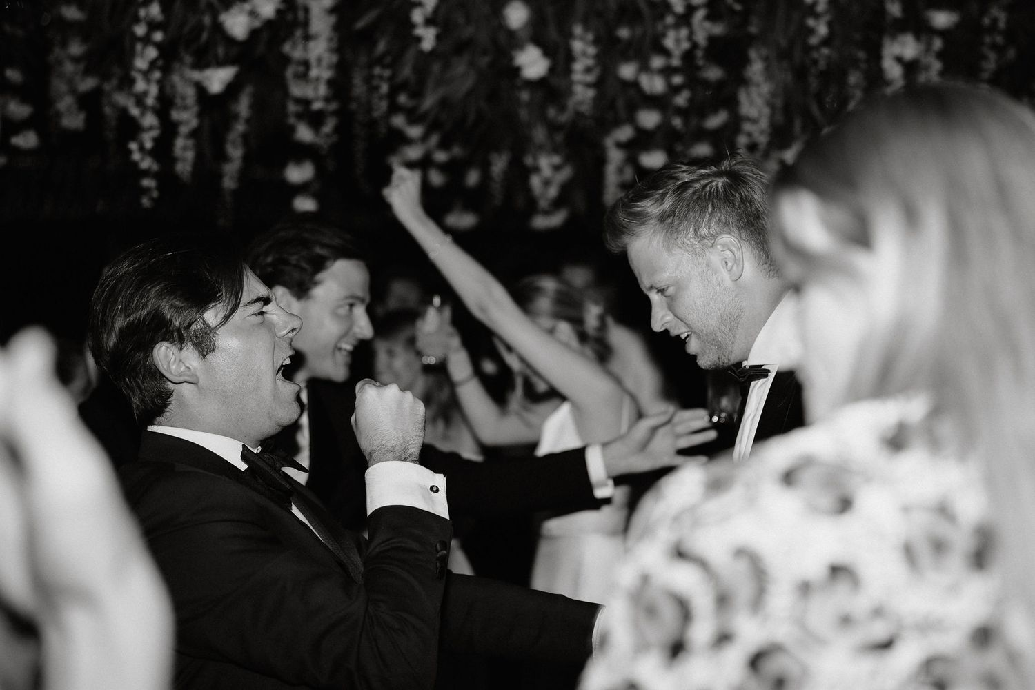 A black and white photo of people dancing at a wedding reception with confetti falling around them.