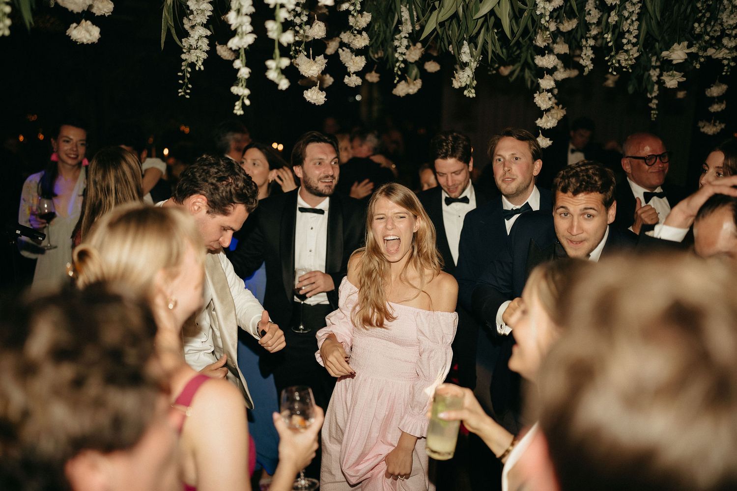 A group of people dancing and celebrating at a lively party or reception on a crowded dance floor.