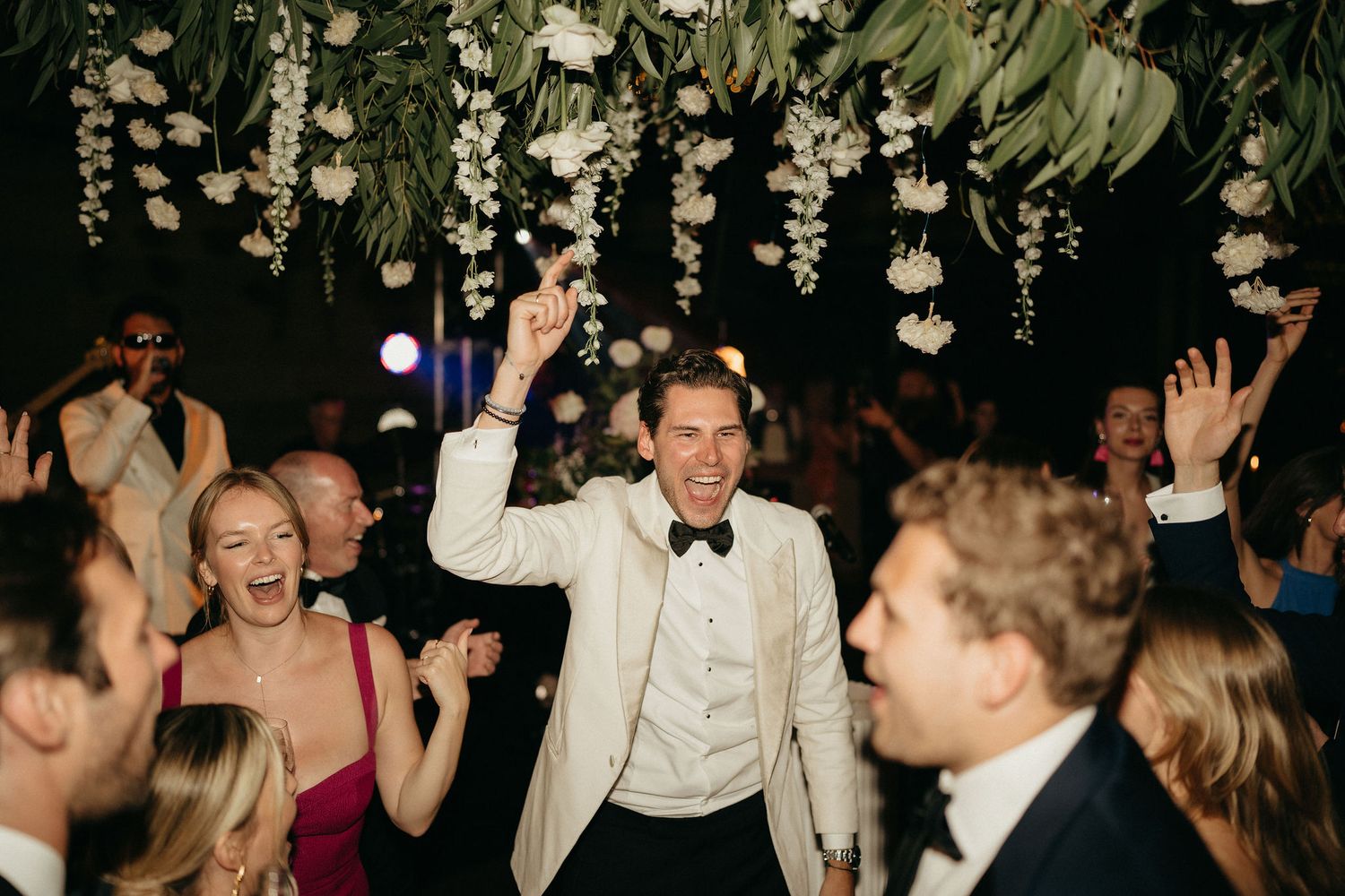 Wedding guests dance and celebrate on a dimly lit dance floor during an evening reception celebration.