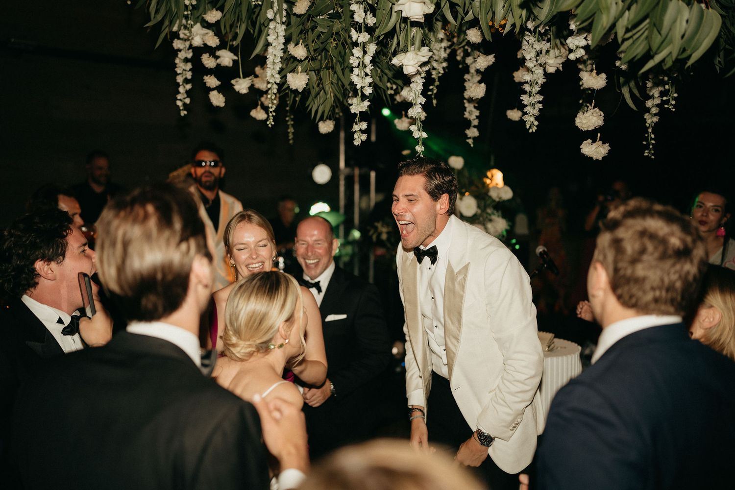 Couples dancing and celebrating together at a dimly lit wedding reception party.