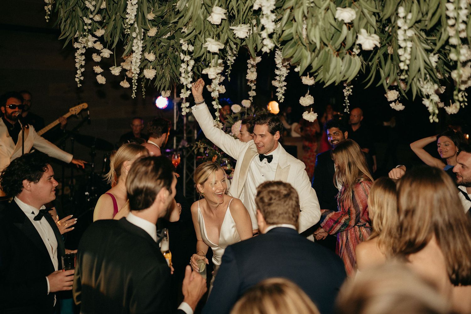 Wedding reception guests dancing under hanging floral decorations at an elegant evening celebration.
