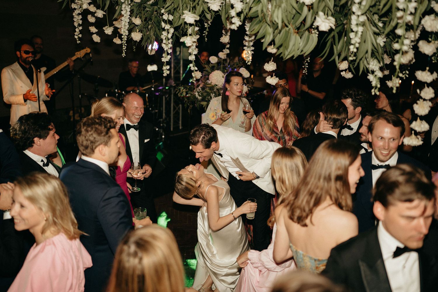 Wedding guests dance and celebrate on a dimly lit dance floor during an evening reception.
