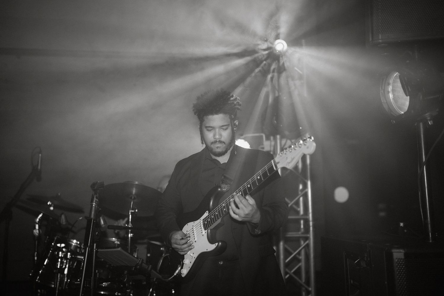 A dramatic black and white concert photo shows a guitarist performing on stage under dramatic lighting.